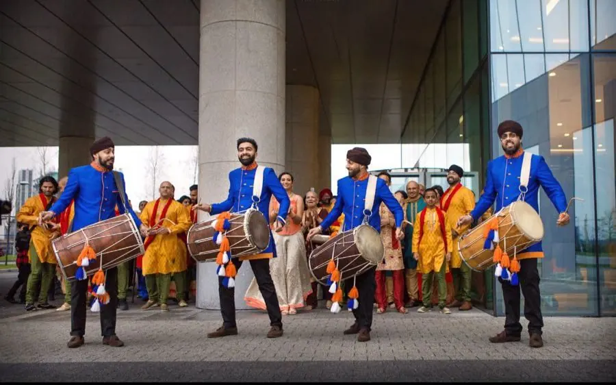 Dhol players in blue jackets leading a baraat outside the InterContinental London, The O2
