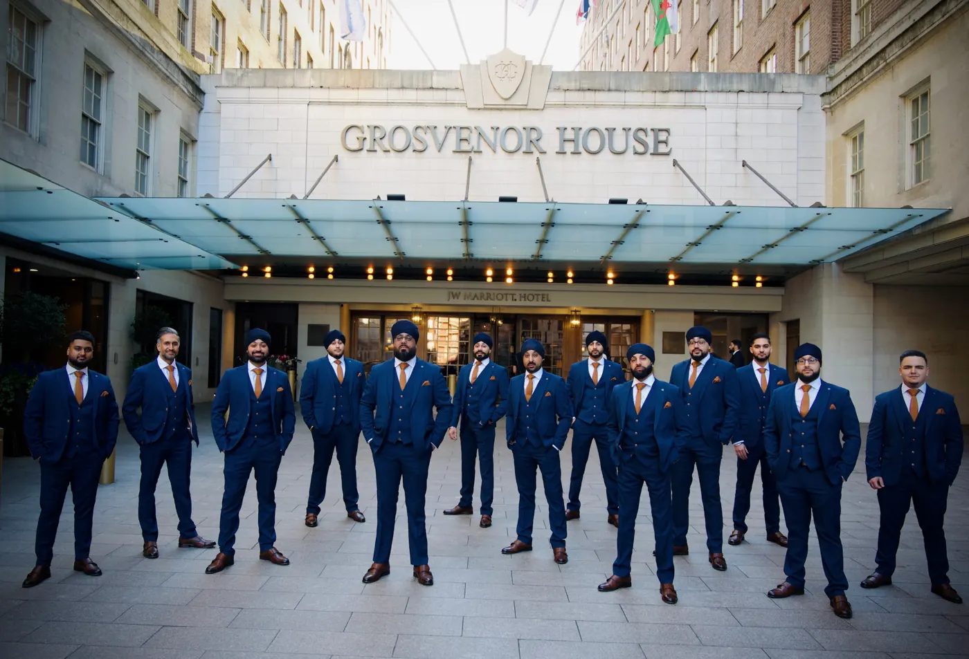 A team of dhol players in navy three-piece suits and turbans outside Grosvenor House, London