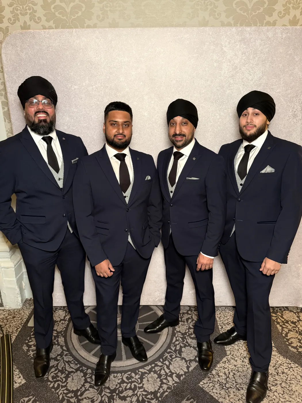 Four dhol players in navy suits, grey waistcoats and black ties